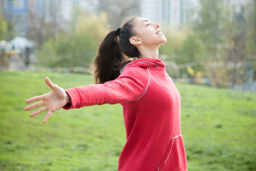 Profile portrait of happy sporty woman relaxing in park. Joyful female model relaxing, breathing fresh air outdoors with opened arms. Healthy active lifestyle concept